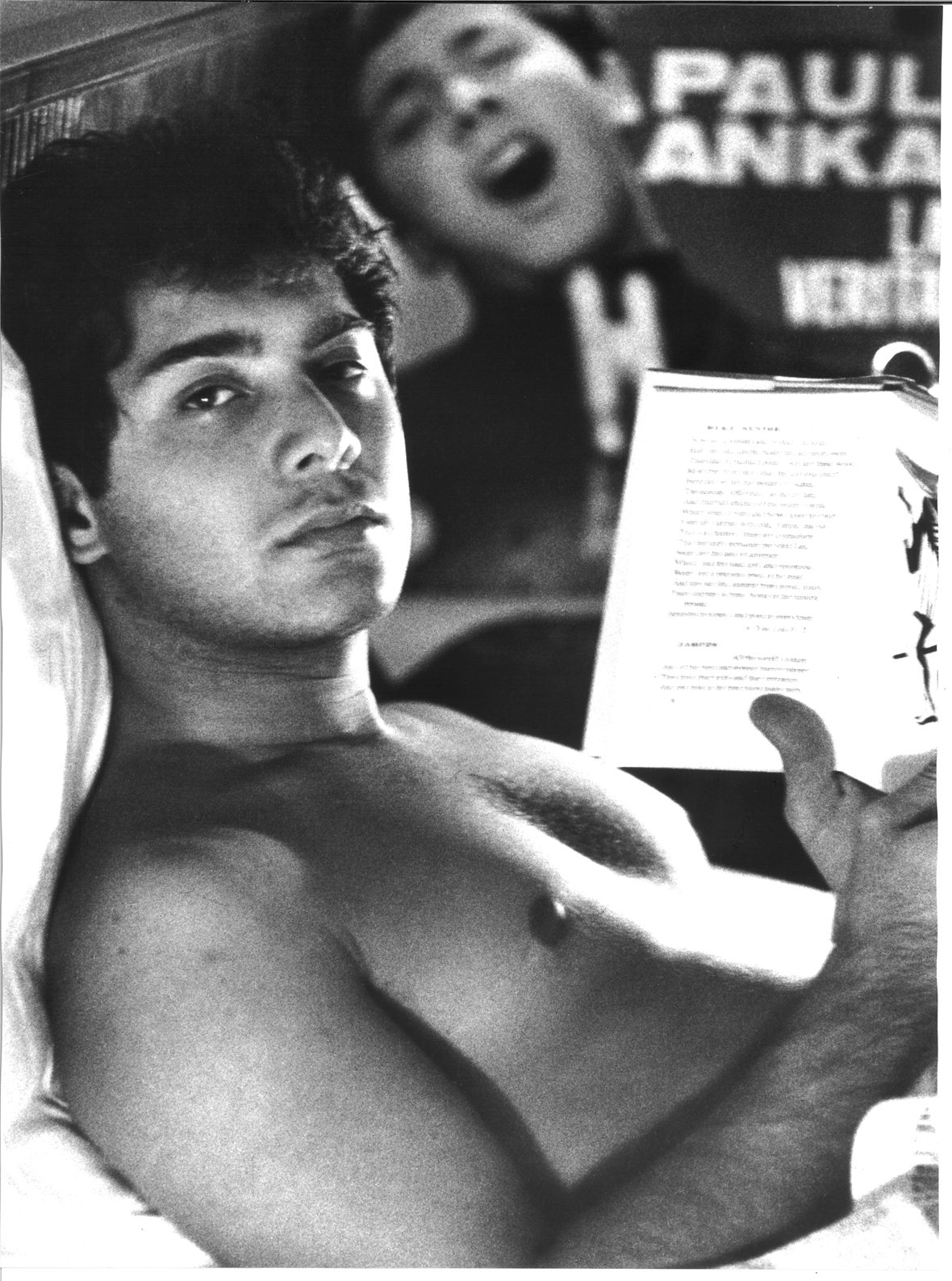 Description: Paul Anka lies in bed reading a book while on tour., Date: (Unknown, 1960s), Photographer: Pietro Pascuttini